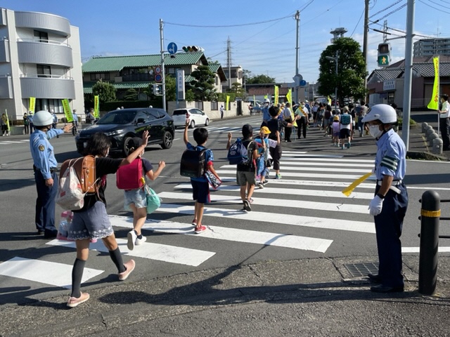 交通指導員が旗を持ち、横断歩道を渡る人を安全に導いている写真